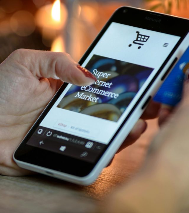 Woman using smartphone for online shopping with credit card in hand, festive background lighting.