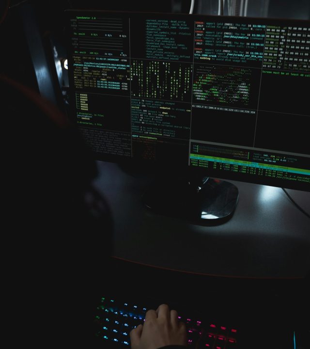 Dark room setup with code displayed on PC monitors highlighting cybersecurity themes.